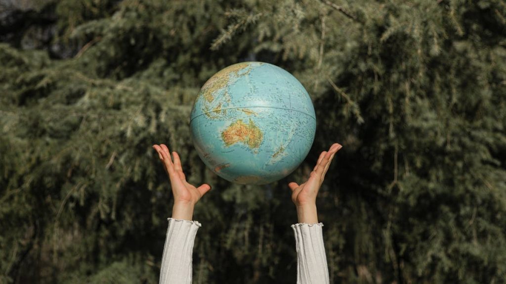 Hands raising a globe against a lush green tree backdrop, symbolizing environmental awareness.