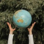 Hands raising a globe against a lush green tree backdrop, symbolizing environmental awareness.
